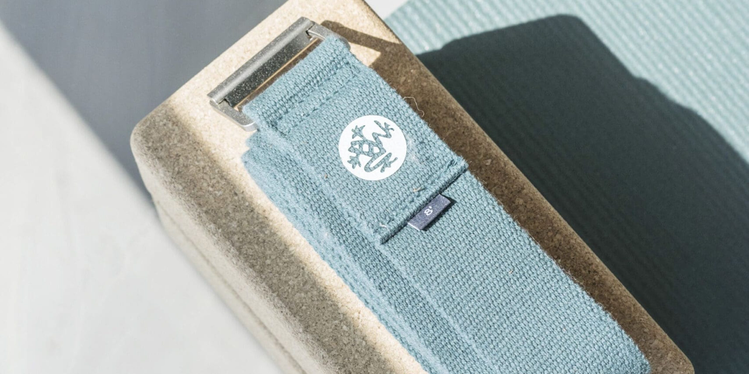 ferielejlighed danmark møllegården ringkøbing fjord En lyseblå yogarem med sølvspænde er pænt placeret oven på en beige yogablok. Remmen har et hvidt logo med et cirkulært design med et stiliseret træ. Baggrunden inkluderer en del af en blågrøn yogamåtte og en skyggefuld, marmoreret overflade.