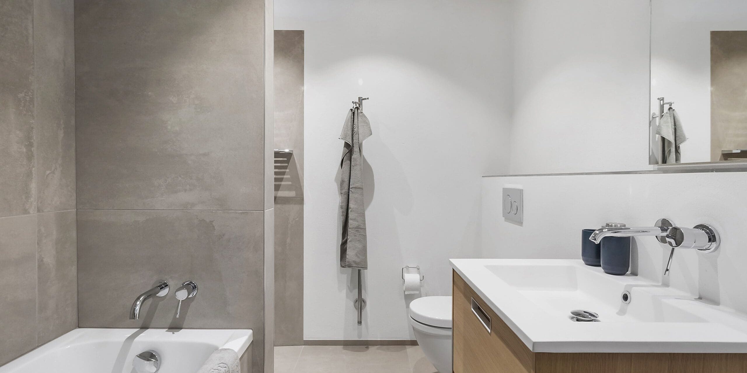 ferielejlighed danmark møllegården ringkøbing fjord Et moderne badeværelse har badekar med vægmonteret vandhane og bruser, toilet og trævask med håndvask. Et stort spejl hænger over forfængeligheden, og væggene er afsluttet med lyse fliser. Håndklæder hænges pænt på kroge.